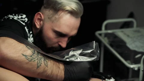 Blond tattoo master with thick black beard makes tattoo Stockbeeldmateriaal 104864242