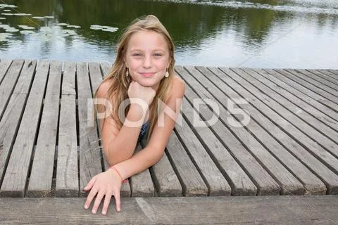 Blond teen girl laying on pier on river Stock Photos