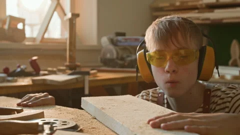 Blond Teenage Boy Blowing Sawdust off Wooden Plank in Woodworking School Stock Footage 334416632
