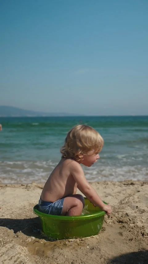 Blond toddler playing in shallow green basin on sandy beach Stock Footage 339459169