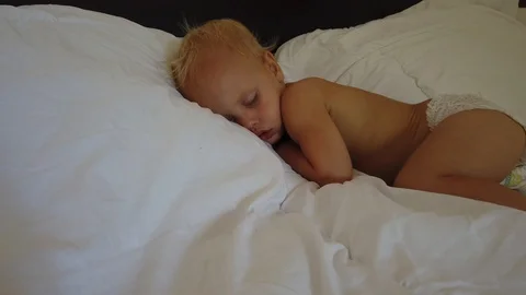  a blond two-year-old child sleeps on a white sheet. Vidéo 107404645