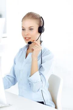 Blond woman call operator is using computer and headset for consulting clients Stock Photos