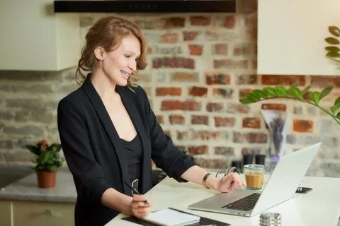A blond woman doing notes in the notebook during a video conference at home. Stock Photos
