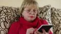 Blond woman with red nails and red lipstick sits on sofa with electronic gadget HD Footage