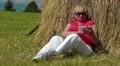 Blond woman sits on green grass near haystack and makes photos on his smartphone HD Footage