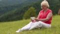 Blond woman sits in the meadow on green grass and talks via skype HD Footage