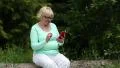 Blond woman sitting on log, holding telephone, earphones, touching screen HD Footage