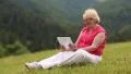 Blond woman sitting in the meadow on green grass and talking on skype HD Footage