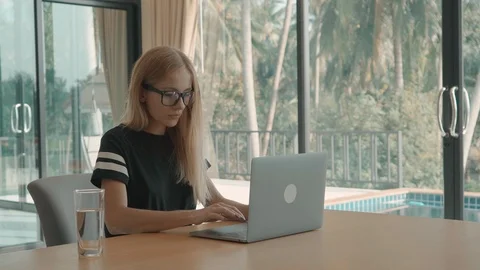 Blond woman types into computer closes it and stretches at her table at home 動画素材 104407407