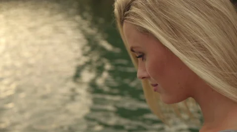 Blond woman's face as she sits beside water. Stock Footage 43637713