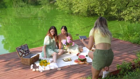 Blond young female is taking photo of her asian friends on picnic Lunch Stock Footage 158886953