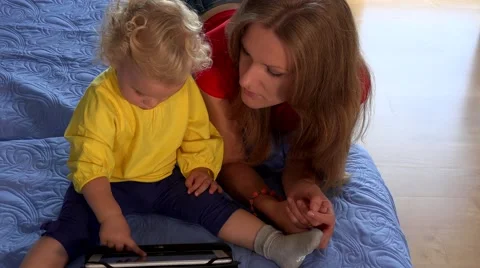 Blonde baby with brunette woman mother using tablet on blue bed Stock Footage