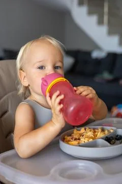A blonde baby eats with a spoon while sitting at a children's dining table Stock Photos