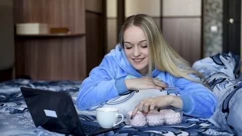 Blonde in bed resting , working in a laptop, eating dessert in daylight Video stock 106697269