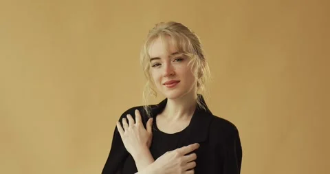 A blonde in a black jacket is looking at the camera on a beige background. Stock Footage 278719105