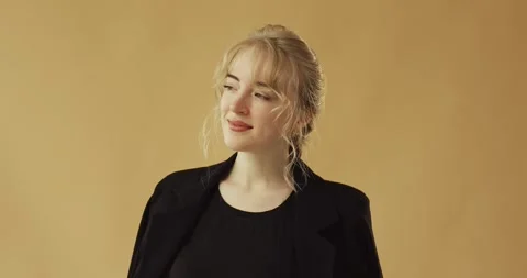 A blonde in a black jacket is looking at the camera on a beige background. Stock Footage 278719154