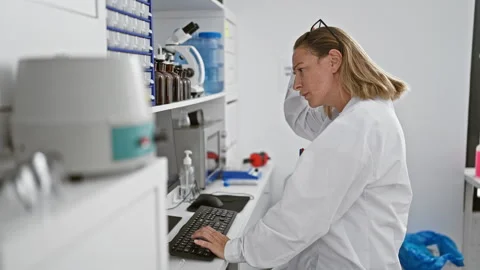 Blonde bombshell in a lab coat, focused, young scientist takes off her glas.. Stock Footage 257105413