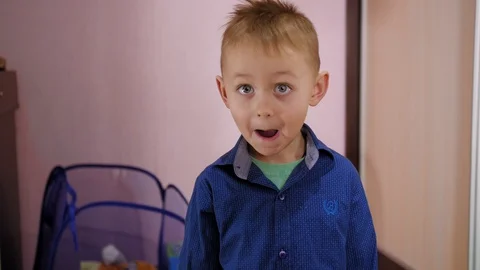 Blonde boy in blue shirt with grey eyes standing in room and looking straight Stock Footage