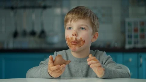 Blonde boy eating Easter chocolate bunnies with dirty face at home on kitchen Stock Footage 127822274
