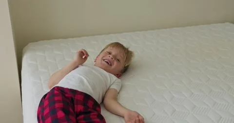 A blonde boy is looking at the camera and smiling while lying on the bed and Stock Footage 324825468
