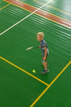 Blonde boy missed while playing badminton in the gym on the green field. Stock Photos