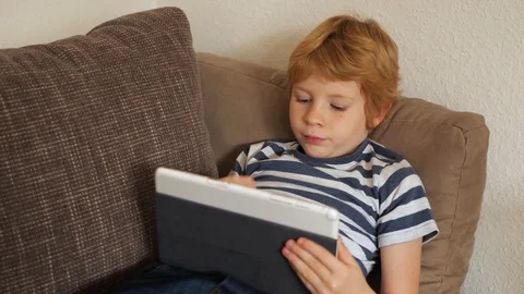 Blonde boy reads something on the tablet. 스톡 동영상 121728670
