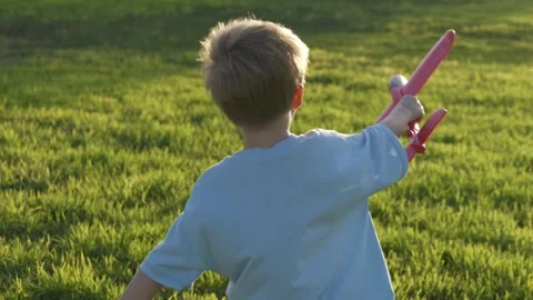Blonde boy runs through the park on green grass holding toy airplane. Active Stock Footage 317317898