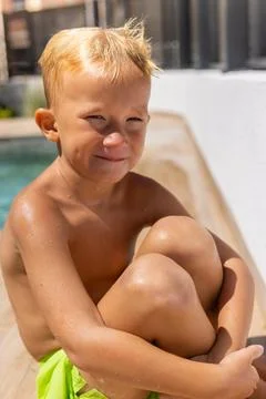Blonde boy sitting poolside after swimming, smiling with joyful expression,.. Stock Photos