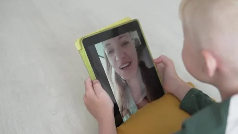 The blonde boy speaks on a tablet by video link with his mother Stock Footage 132553493