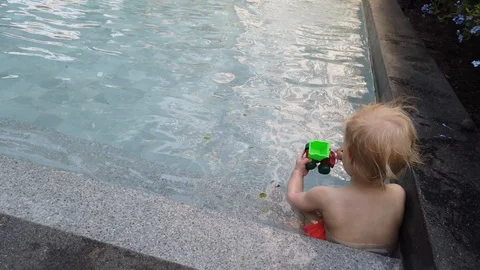 Blonde boy of two years playing with a toy, sitting in the pool.  Stock Footage 104698319