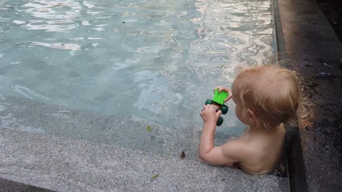 Blonde boy of two years playing with a toy, sitting in the pool.  Stock Footage 104698336