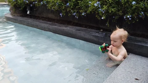 Blonde boy of two years playing with a toy, sitting in the pool.  Vidéo 104698377