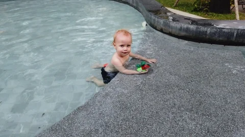 Blonde boy of two years playing with a toy, sitting in the pool.  Stock Footage 104698566