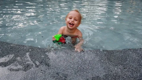 Blonde boy of two years playing with a toy, sitting in the pool.  Stock Footage 104698695