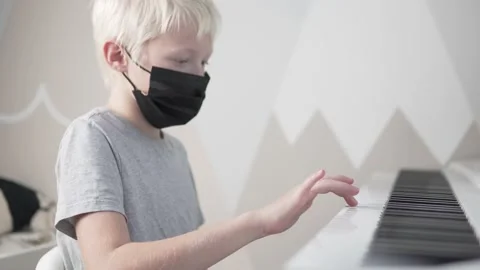 A blonde boy wearing a face mask learns to play the piano at school during the Stock Footage 164330393