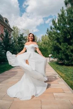 A blonde bride dancing on a path in the park in a white long dress. Foto stock