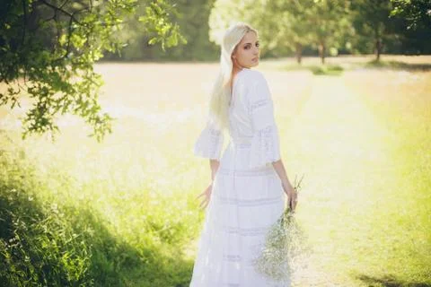 Blonde bride standing in tree shadow looking over shoulder Stock Photos