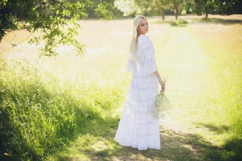 Blonde bride standing in tree shadow looking over shoulder Stock Photos