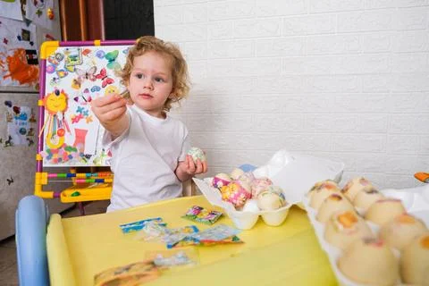 Blonde child decorating egg for Easter holiday. Little kid holding festive decal Stock Photos