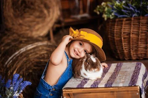 Blonde cute girl smiling in a straw hat holding a rabbit, rustic style, happy Stock Photos