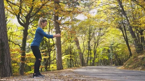 Blonde does squats on empty rural road side in autumn forest Stock Footage 156655065