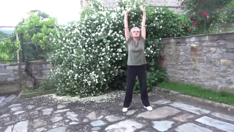 Blonde doing squats tai chi and raising her arms in her backyard Vídeos de archivo 336398635