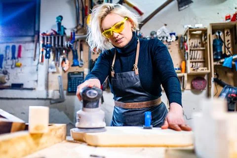 Blonde female carpenter using tools for her work in a woodshop Stock Photos