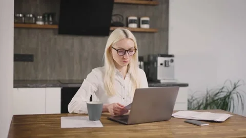 A blonde freelancer working at a laptop in the kitchen. Sorts through documents Stock Footage 171962885