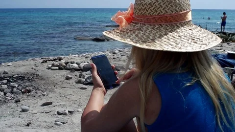 A blonde girl with hat using her mobile phone at beach Stock Footage 108232665