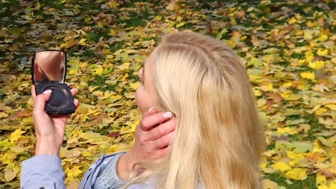 Blonde girl preening while looking in the mirror in the park Stock Footage 292959432