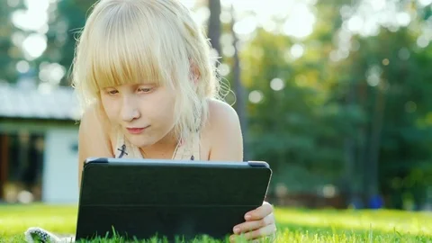 Blonde girl uses a tablet. Lying on the grass in the backyard of the house Stock-Footage 80026341