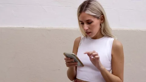 A blonde girl using her smart phone on a background wall. Stock Footage 211155326