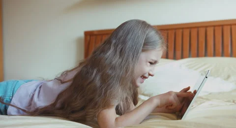 Blonde girl using tablet pc on the bed. Child 6-8 years lying on the bed Video stock 55883317