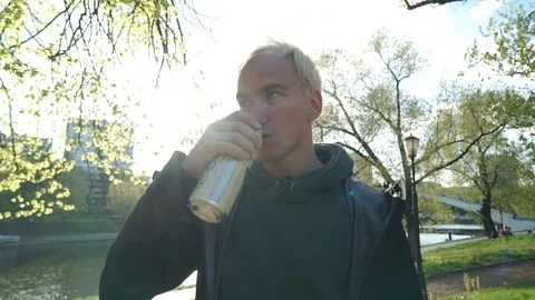 Blonde guy drinking a beer on park background Stock Footage 107788824